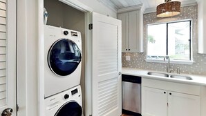 Un lavadero con dos lavadoras apiladas y un lavavajillas, un lavabo y una ventana con vistas al exterior.