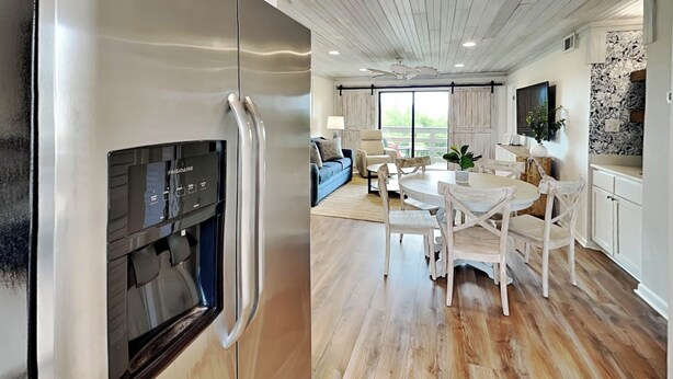 Una cocina moderna con un refrigerador de acero inoxidable, un dispensador de agua y un comedor con una mesa redonda y sillas blancas.