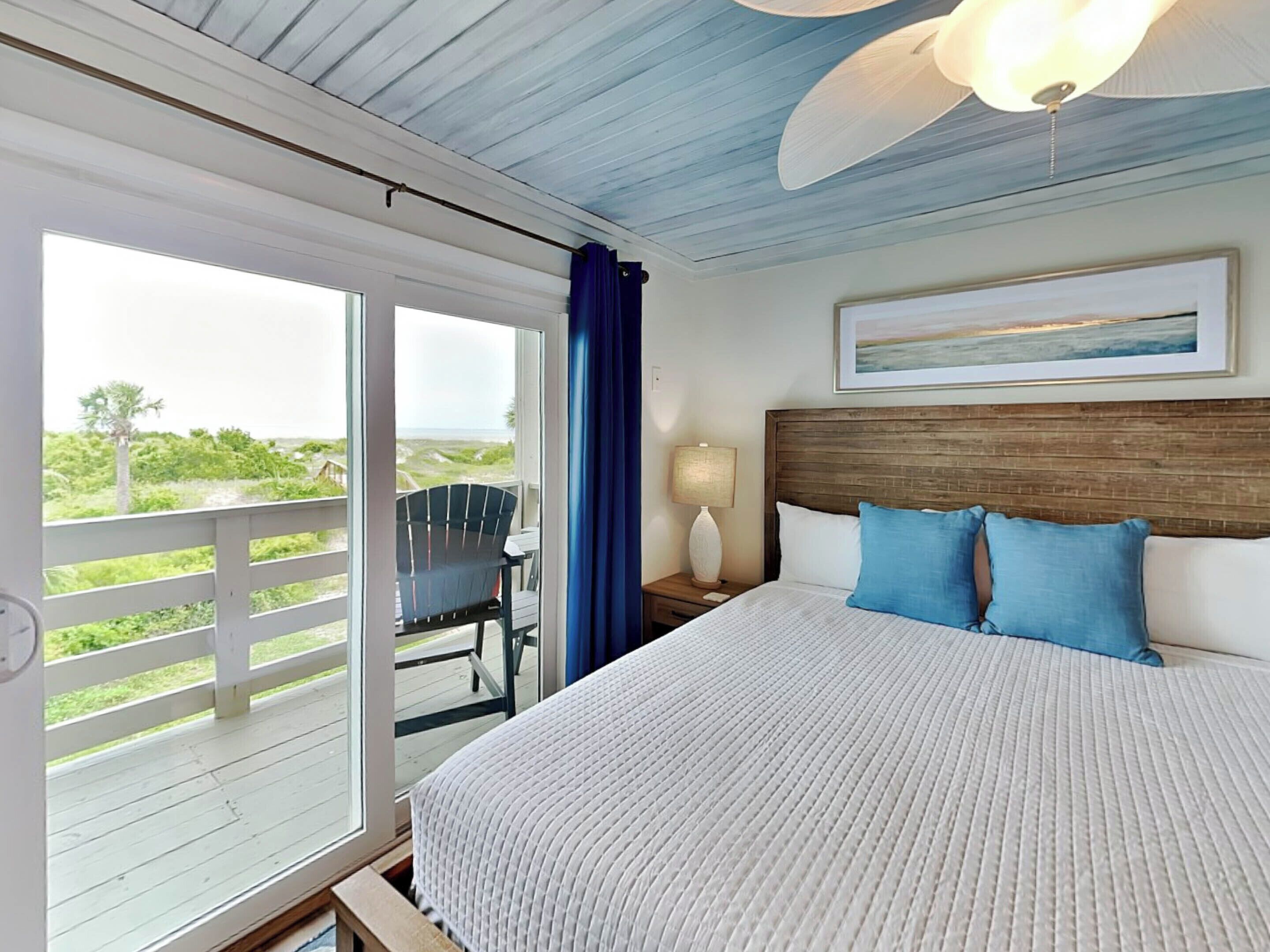 A bedroom with a large bed, a nightstand, a chair, and a view of the outdoors.