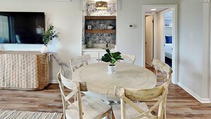 Un área de comedor con una mesa redonda y seis sillas de madera, un televisor a la izquierda y un papel tapiz detrás de la barra.