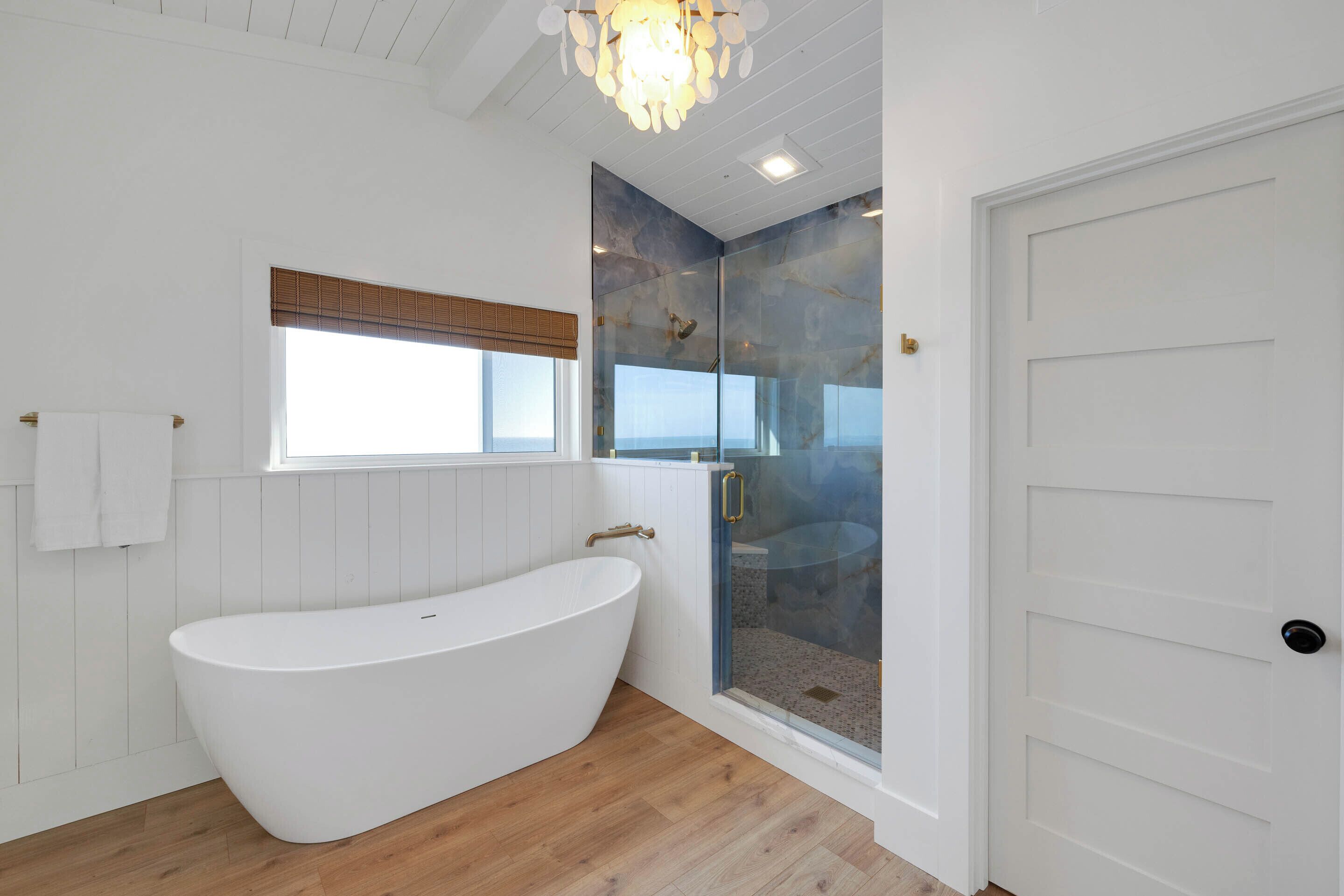 Un baño moderno con una bañera independiente, cabina de ducha con mampara de vidrio y una puerta blanca.