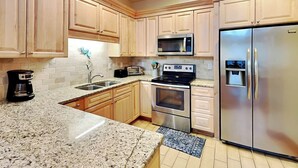 A kitchen with wooden cabinets, granite countertops, stainless steel appliances, and a built-in microwave. - The Gardens 703 by Tybee Vacation Rentals (Tybee Island)