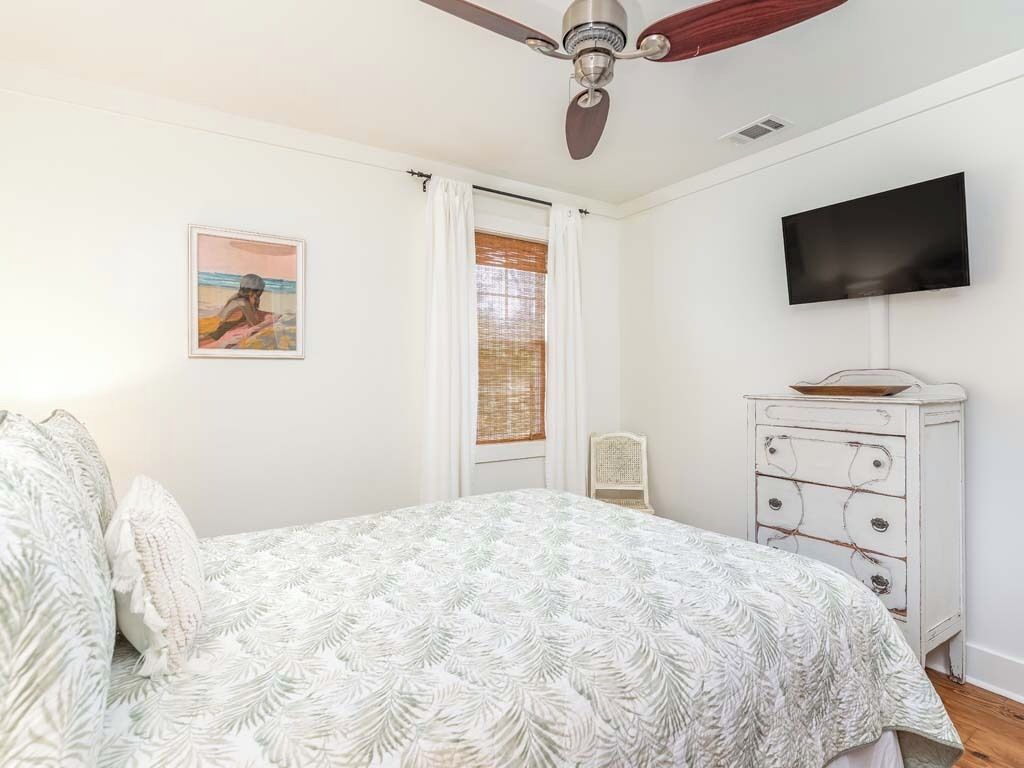 A bedroom with a bed, a ceiling fan, a television, and a dresser.