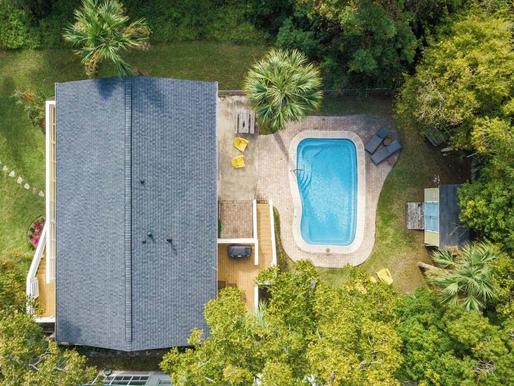 Luchtbeeld van een woonhuis met een zwembad, een overdekt terras en een groot huis met een donker dak.