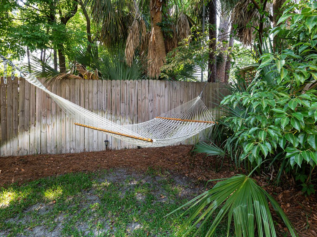 A hammock in a garden with a wooden fence and lush greenery.