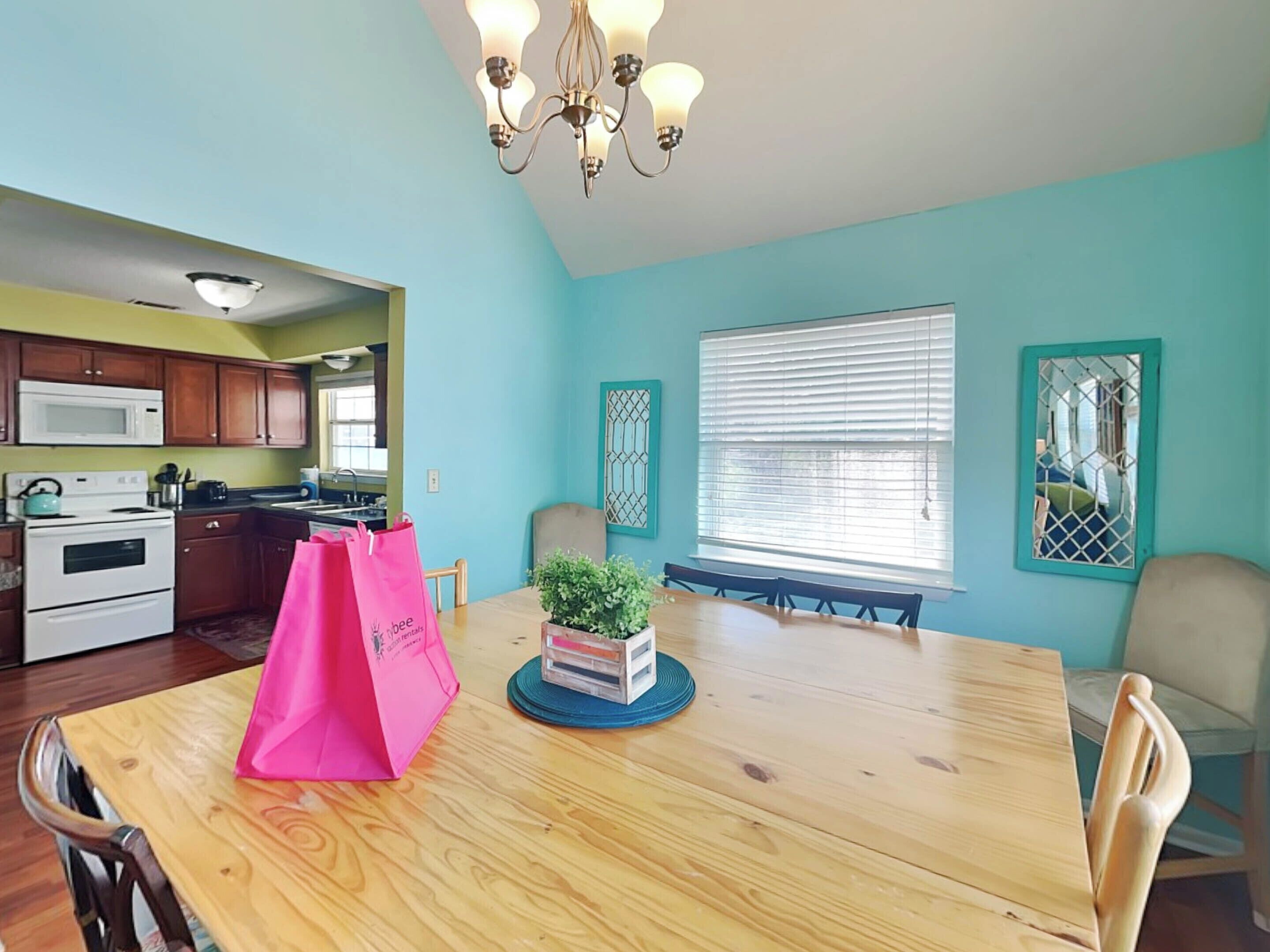 A dining area with a wooden table, chairs, a pink bag, and a potted plant.