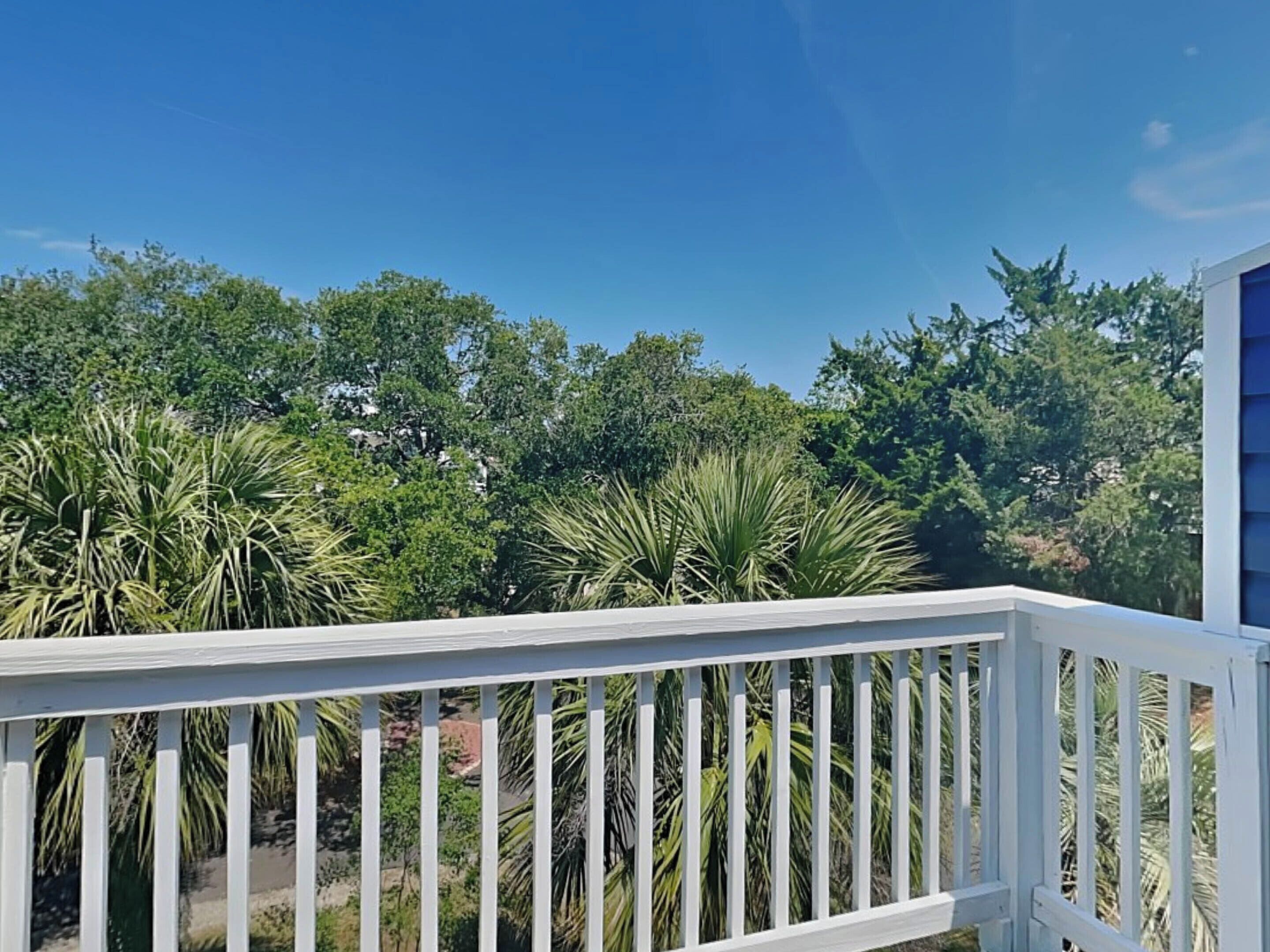 A white balcony railing with a view of dense green foliage and trees in the background.