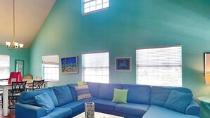 Un salon spacieux avec un canapé d’angle bleu, une table basse blanche et un coin repas comprenant une table et des chaises.