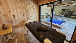 Een spa ruimte met een massagetafel, houten wanden en uitzicht op een buitenzwembad.