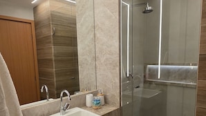 A modern bathroom with a glass-enclosed shower, a large mirror, and a vanity with a sink and storage. - Flat Luxo e Conforto 224 Eco Resort by La Playa (Tamandaré)