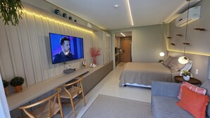A modern hotel room with a flat-screen TV, a desk with chairs, a bed, a sofa, and a bedside table with a lamp. - Flat Luxo e Conforto 224 Eco Resort by La Playa (Tamandaré)