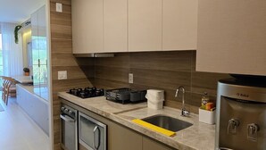 A modern kitchen with a built-in stove, oven, and dishwasher. There is a large window providing natural light and a view of the outdoors. - Flat Luxo e Conforto 224 Eco Resort by La Playa (Tamandaré)