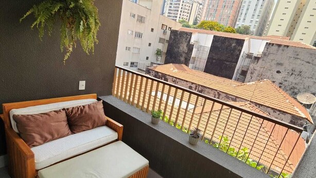 A balcony with a wooden sofa, a potted plant, and a view of neighboring buildings. - In Perdizes, a very well-equipped studio apartment near Allianz Parque and PUC university. (City of Sao Paulo)