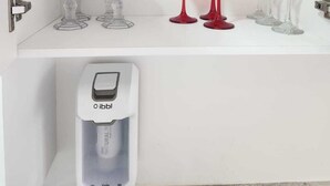 A bathroom with a white sink, a mirror, and a shelf with various glassware including two red wine glasses and several clear glasses. - In Perdizes, a very well-equipped studio apartment near Allianz Parque and PUC university. (City of Sao Paulo)