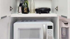 A kitchen with a white microwave, a blender, a bottle of olive oil, and a glass bottle. - In Perdizes, a very well-equipped studio apartment near Allianz Parque and PUC university. (City of Sao Paulo)