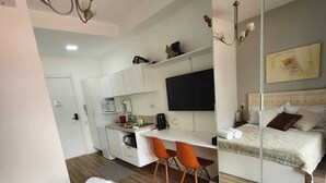 A modern hotel room with a bed, a desk, a chair, a mirror, and a television. - In Perdizes, a very well-equipped studio apartment near Allianz Parque and PUC university. (City of Sao Paulo)