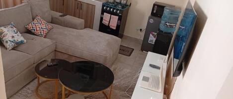 A compact living space with a sofa, two coffee tables, a kitchenette, and a water dispenser.