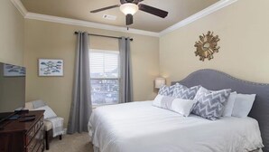 Un dormitorio con cama, ventilador de techo, cómoda, escritorio y ventana con cortinas.