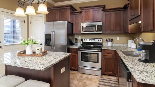 Una cocina con gabinetes de madera oscura, electrodomésticos de acero inoxidable, encimeras de granito y una isla central con un jarrón de flores.