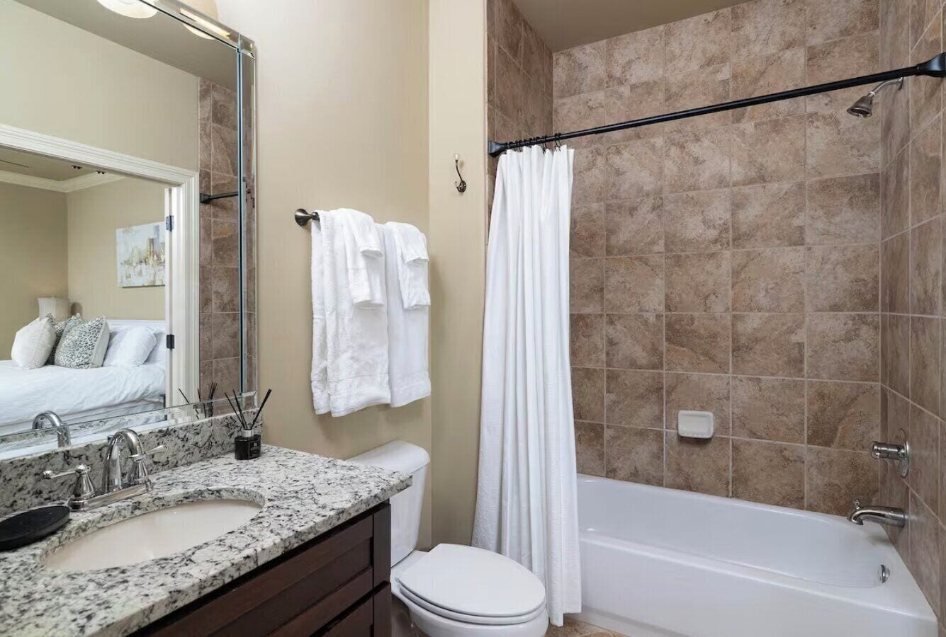 A bathroom with a marble sink, a toilet, a bathtub, and a shower curtain.
