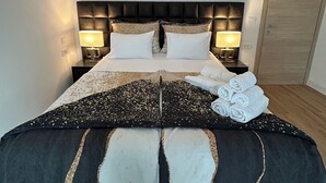 A neatly made bed with a dark headboard, two bedside lamps, and a stack of towels on the side.