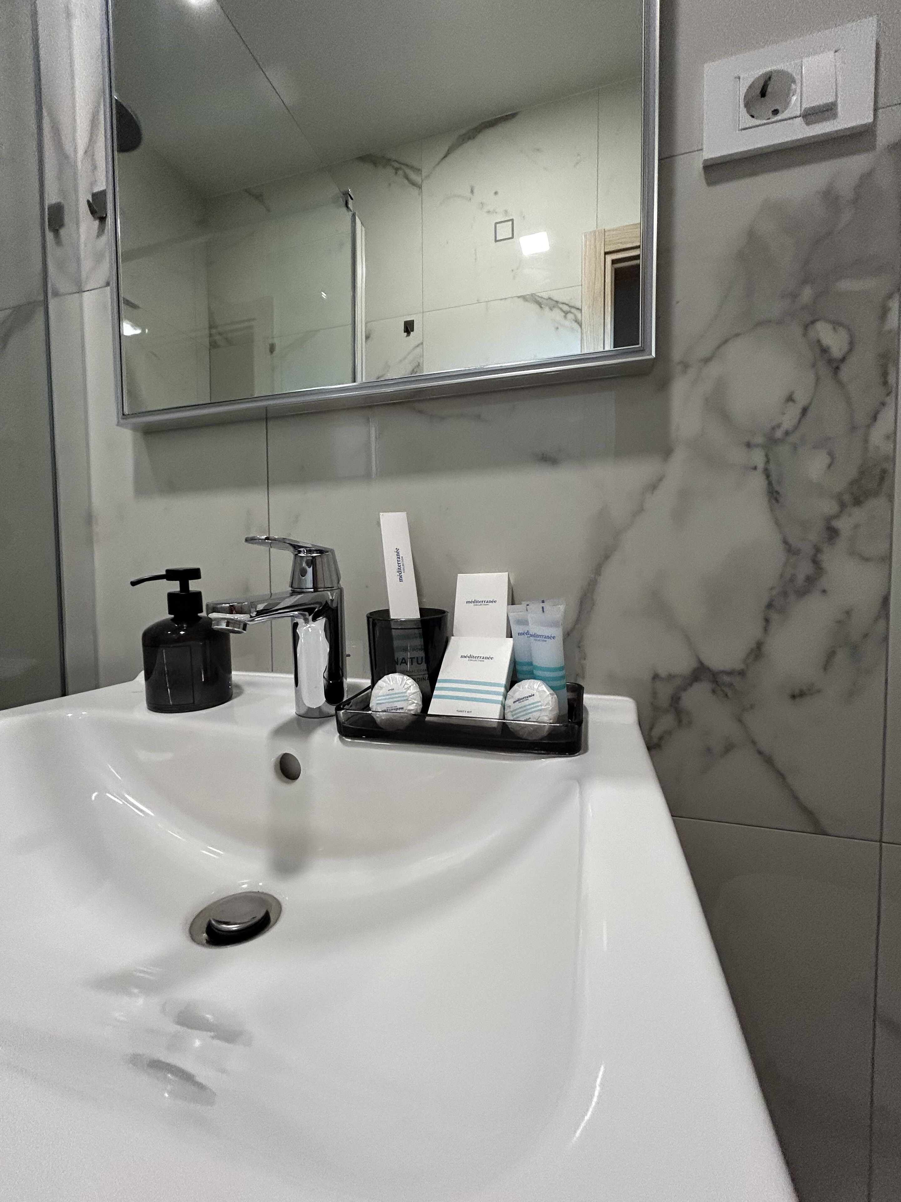 Et badeværelse med en hvid vask, et spejl og toiletartikler på vasken.