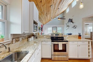 Cucina con mobili bianchi, piano di lavoro in granito, piano cottura in acciaio inossidabile e ventola a soffitto.