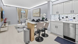 A modern kitchen with a dining area, white cabinetry, a stainless steel dishwasher, and a small island with bar stools.