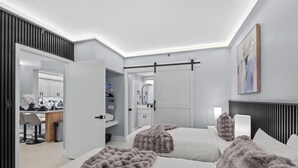 A modern bedroom with two beds, a large mirror, and a view into the adjacent bathroom.