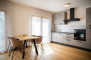 A modern kitchen with wooden cabinets, a built-in oven, and a dining area with a table and chairs. - 735 Apartment Julia (Merano)