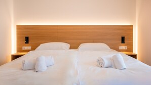 A double bed with white linens and towels, wooden headboard, bedside lamps, and a wall socket.