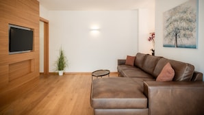 A modern living room with a brown leather sofa, a small round table, a potted plant, and a flat-screen TV mounted on a wooden wall. - 735 Apartment Julia (Merano)
