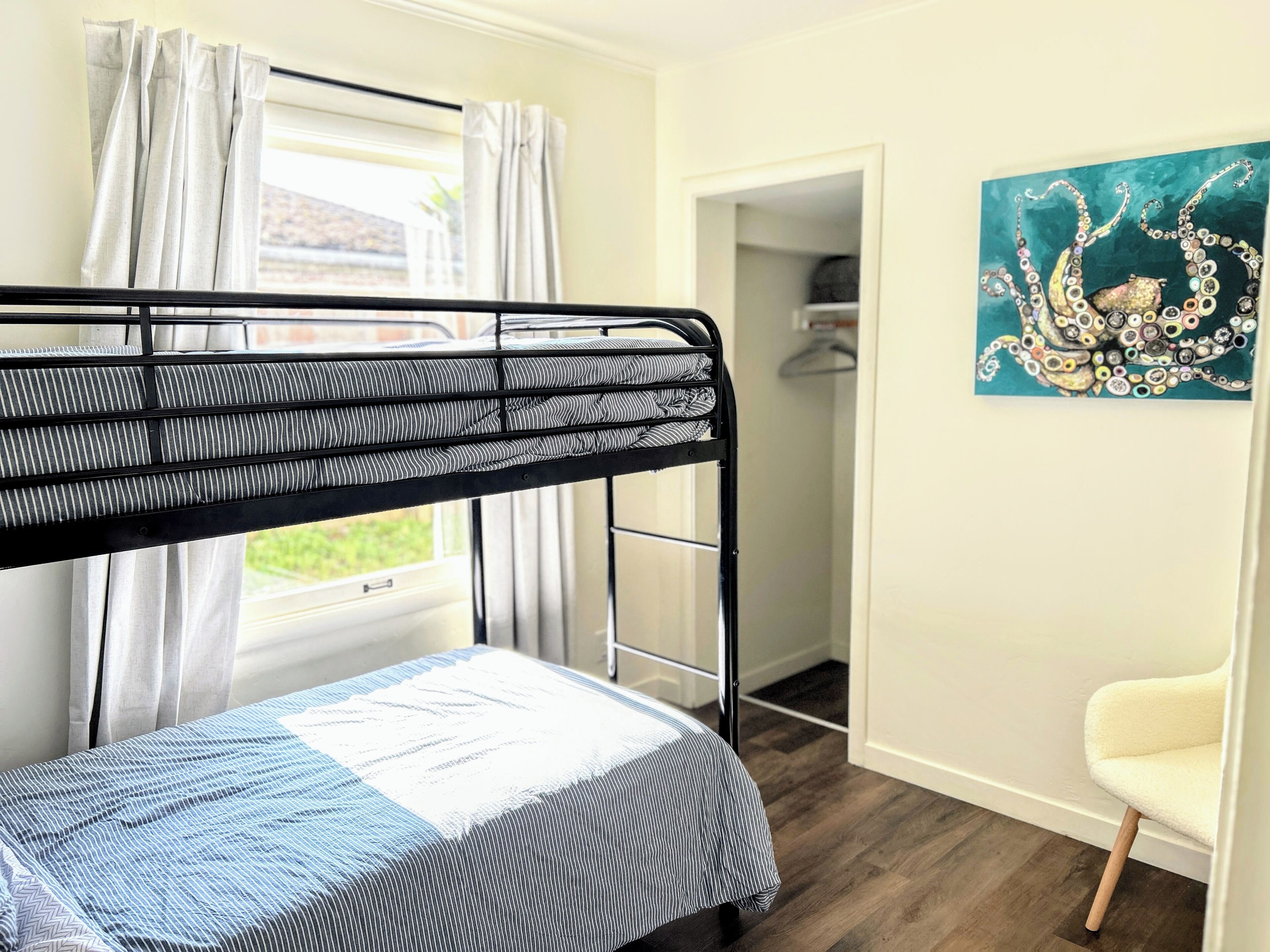 A bunk bed with a striped mattress, a white chair, and a painting on the wall.