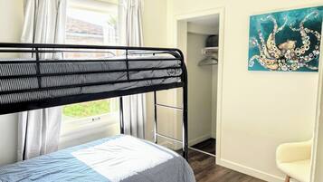 A bunk bed with a striped mattress, a white chair, and a painting on the wall.