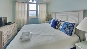 Een slaapkamer met een groot bed, een televisie op een dressoir en een raam met gordijnen.