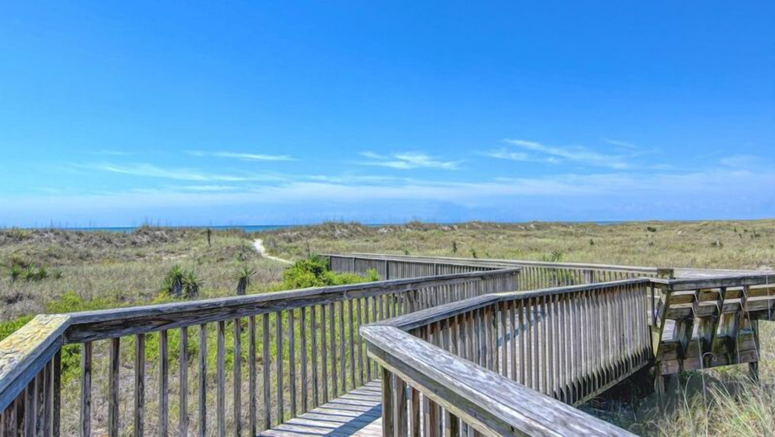 A wooden boardwalk leading to a beach with a clear sky.