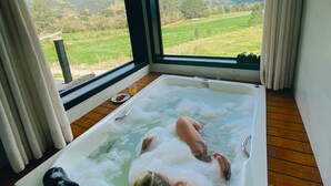 A person relaxing in a hot tub with a view of a green landscape and mountains. - Refúgio Serra e Flor (Urubici)