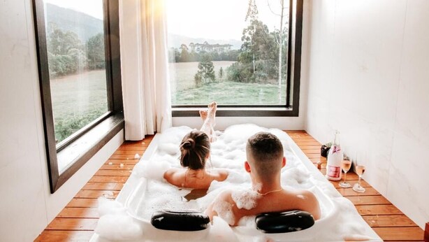 A room with a large window, a wooden floor, and a bathtub filled with bubbles. - Refúgio Serra e Flor (Urubici)