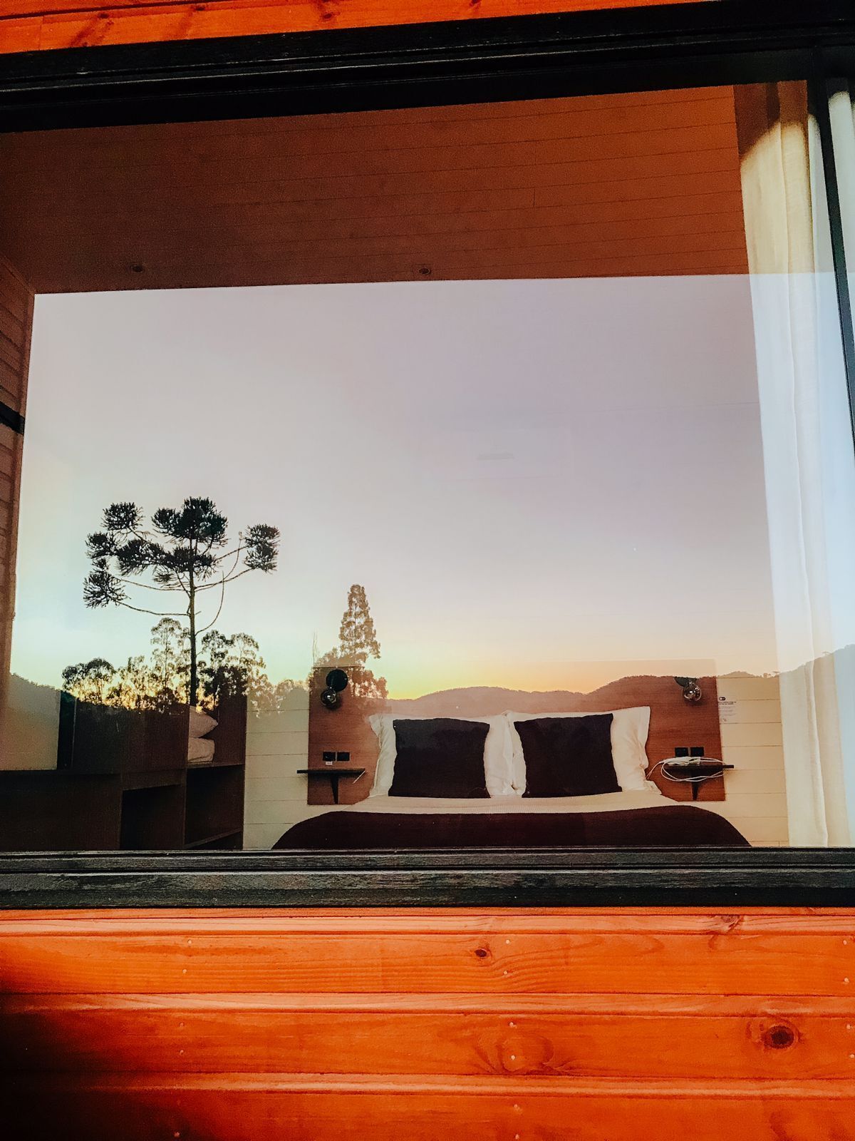 Ein Schlafzimmer mit Bett, Nachttisch und Blick auf Bäume und Hügel.