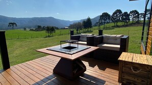 A wooden deck with a built-in table and outdoor seating, overlooking a green landscape and mountains. - Refúgio Serra e Flor (Urubici)
