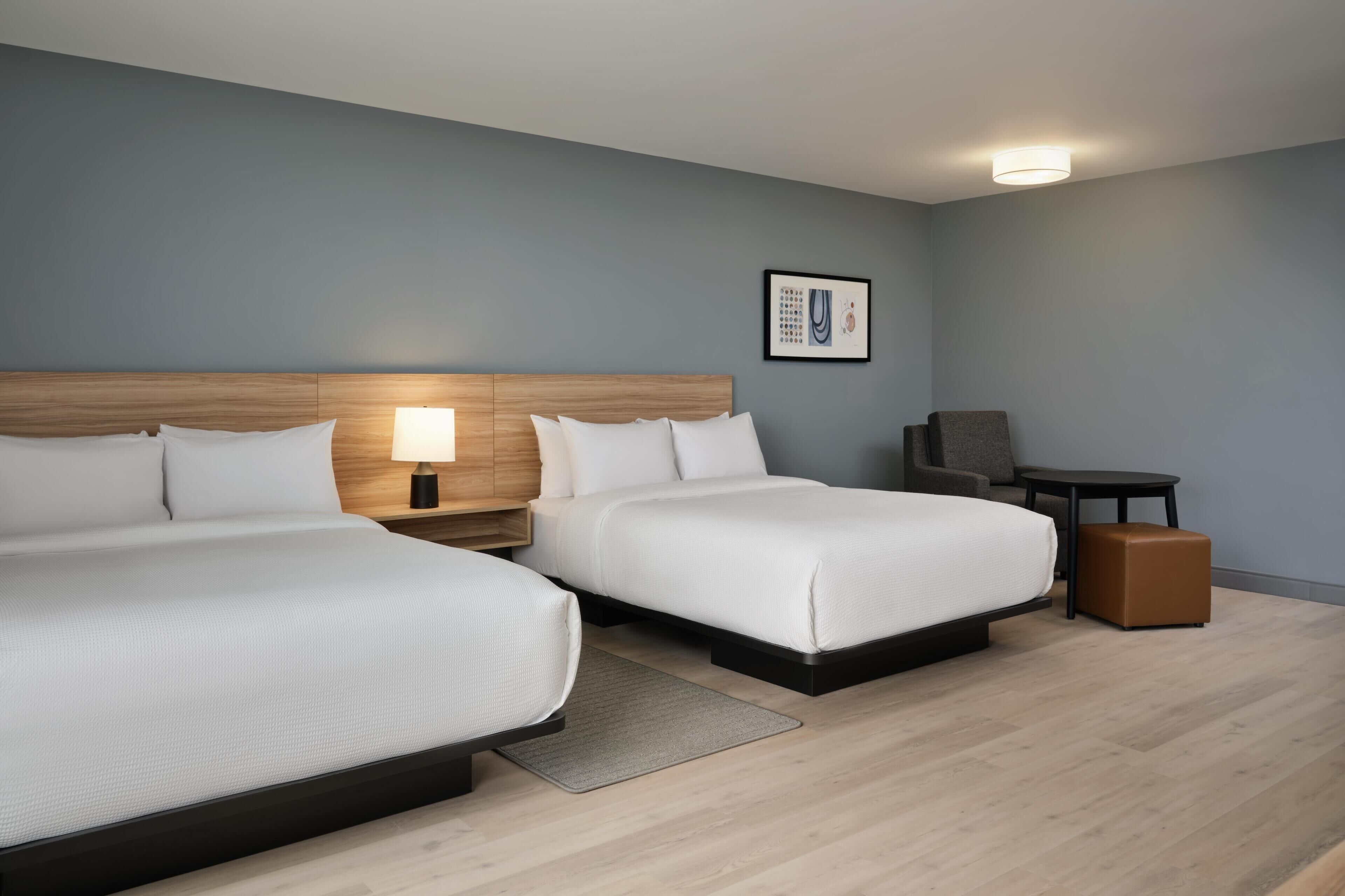 Une chambre d’hôtel avec deux lits, un bureau, une chaise et une petite table.