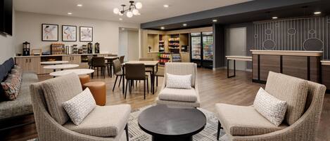 A modern lounge area with sofas, a coffee station, and a counter with snacks.