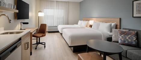 Camera d'albergo con un letto, una poltrona, una scrivania con lampada, una TV e una finestra con tende.