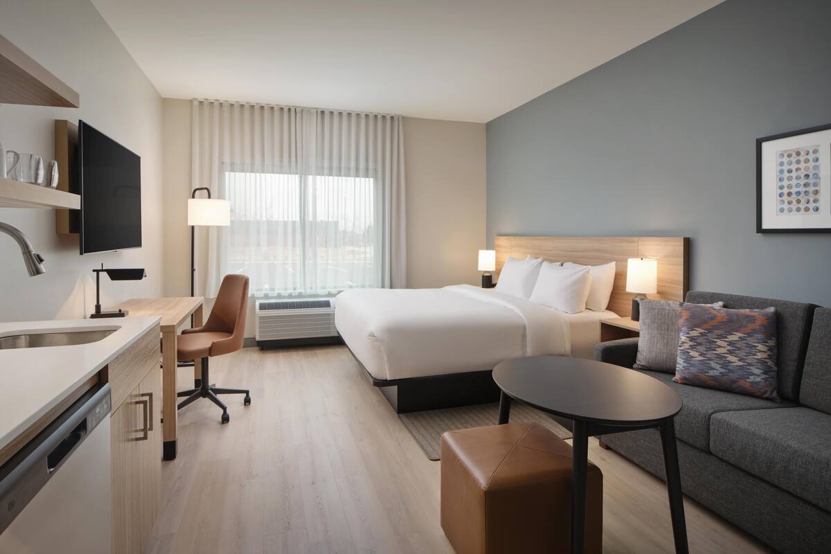 Une chambre d’hôtel moderne équipée d’un lit, d’un canapé, d’un bureau avec une chaise, d’une télévision et d’une fenêtre avec des rideaux.