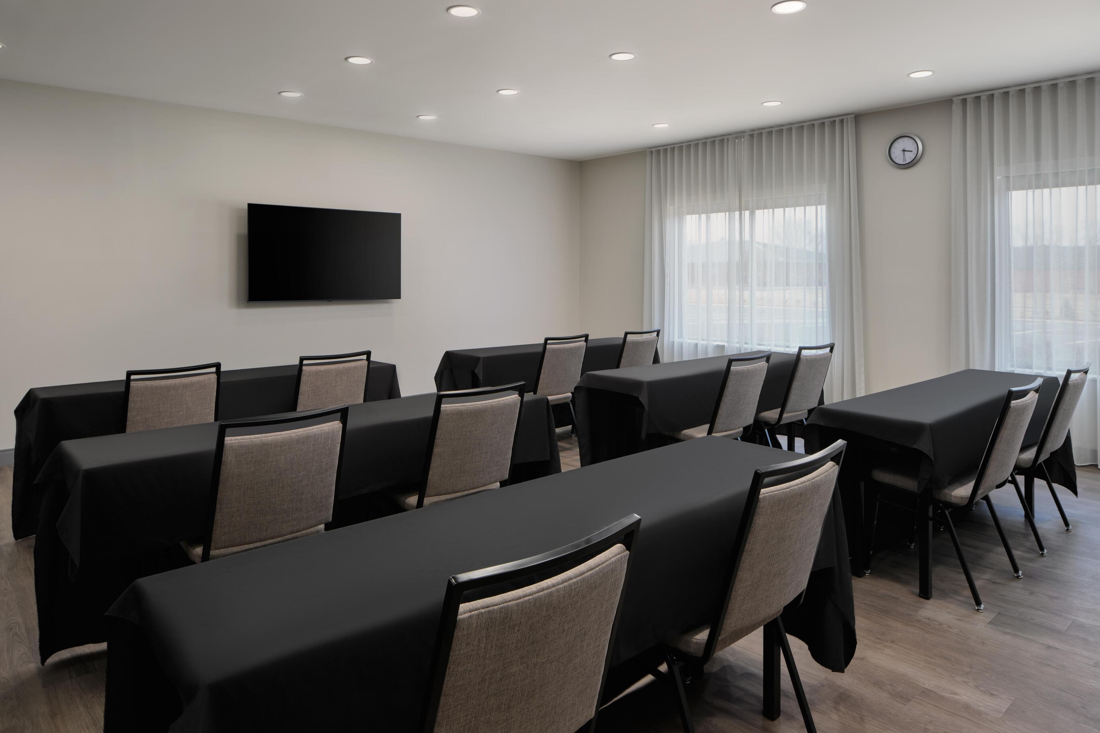 A conference room with multiple tables and chairs, a flat-screen TV mounted on the wall, and a clock on the wall.