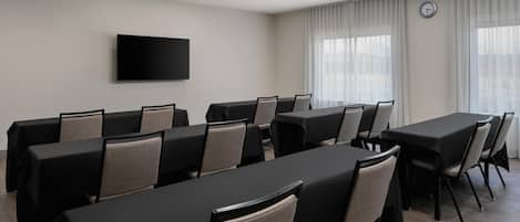 A conference room with multiple tables and chairs, a flat-screen TV mounted on the wall, and a clock on the wall.