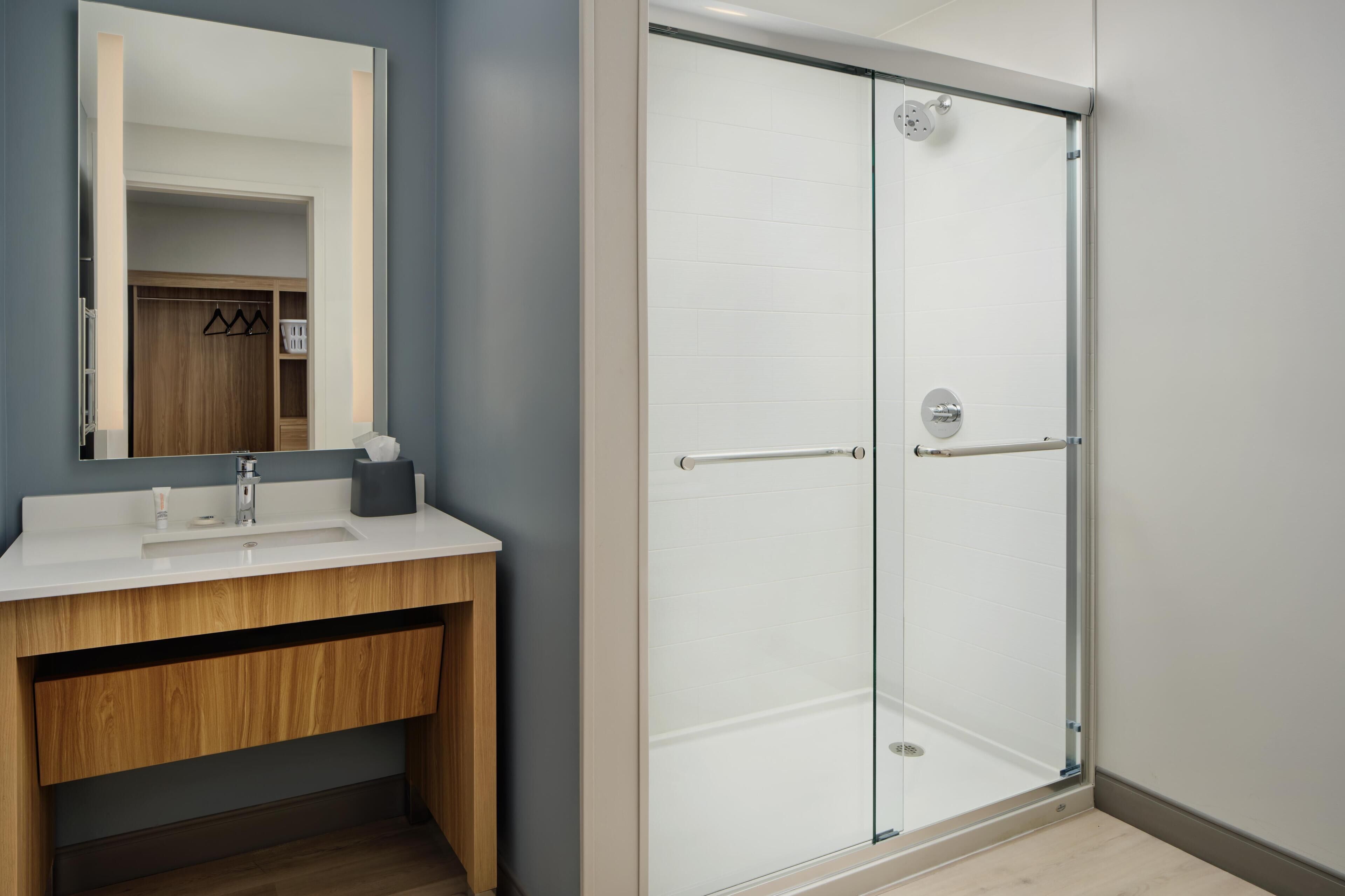 Une salle de bain moderne avec une douche à parois de verre, un meuble-lavabo en bois et un miroir au-dessus du lavabo.