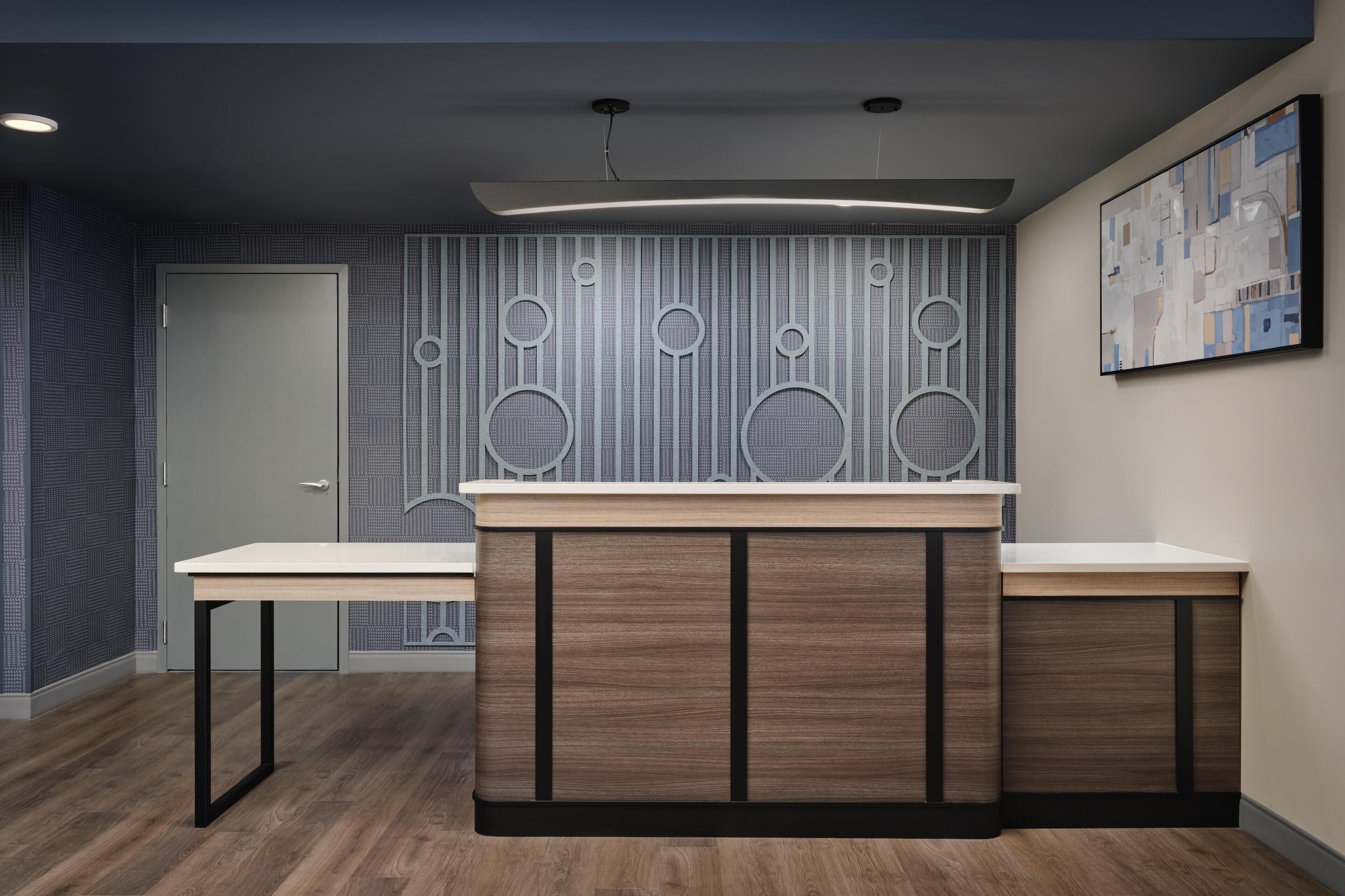 A reception area with a wooden reception desk, a patterned wall, and a framed abstract painting.