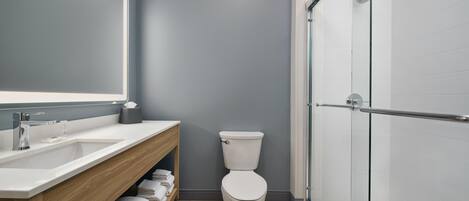 A modern bathroom with a white sink, wooden vanity, and a glass shower enclosure.