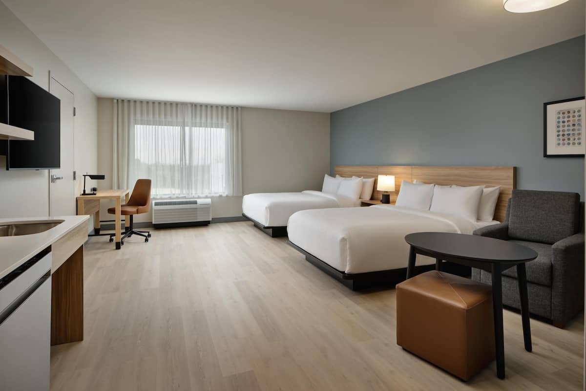 Une chambre d’hôtel avec deux lits, un bureau, une chaise, une petite table et un téléviseur.